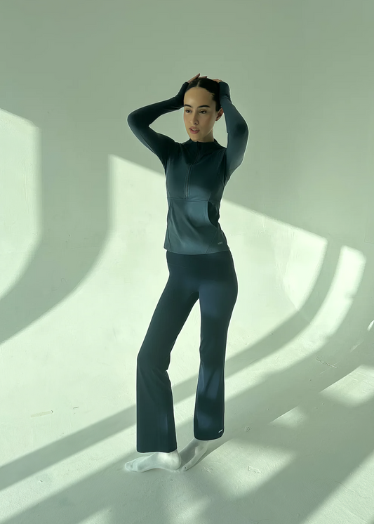 Person wearing a dark outfit standing in a well-lit room with shadows on the floor.