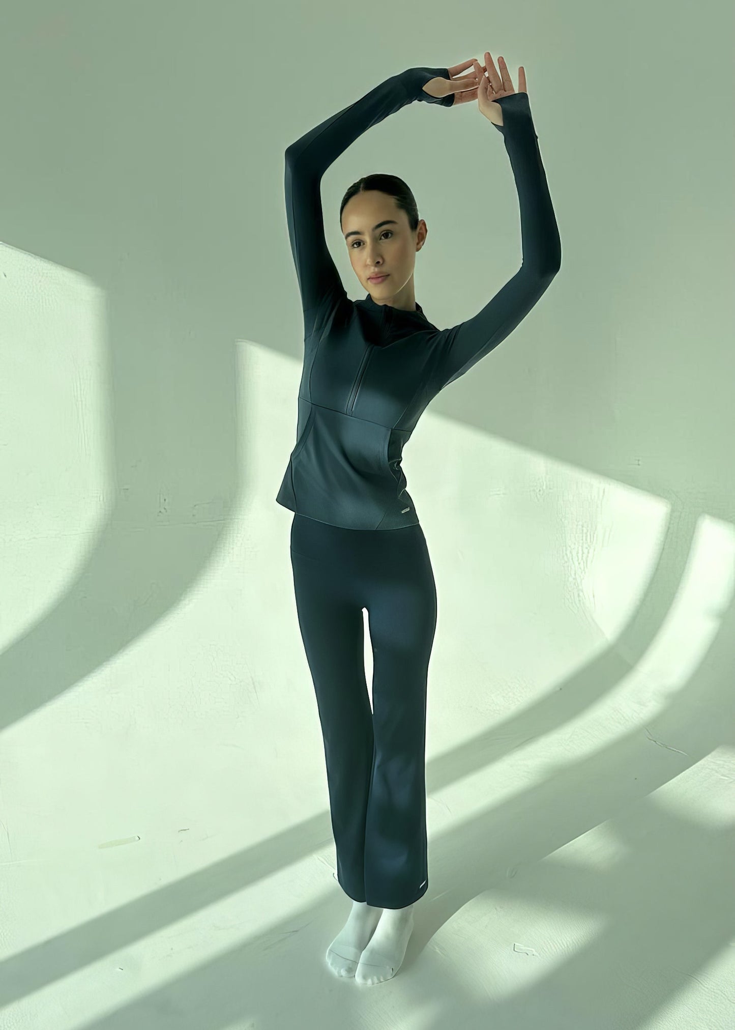 Person in a black outfit standing with one arm raised against a white background
