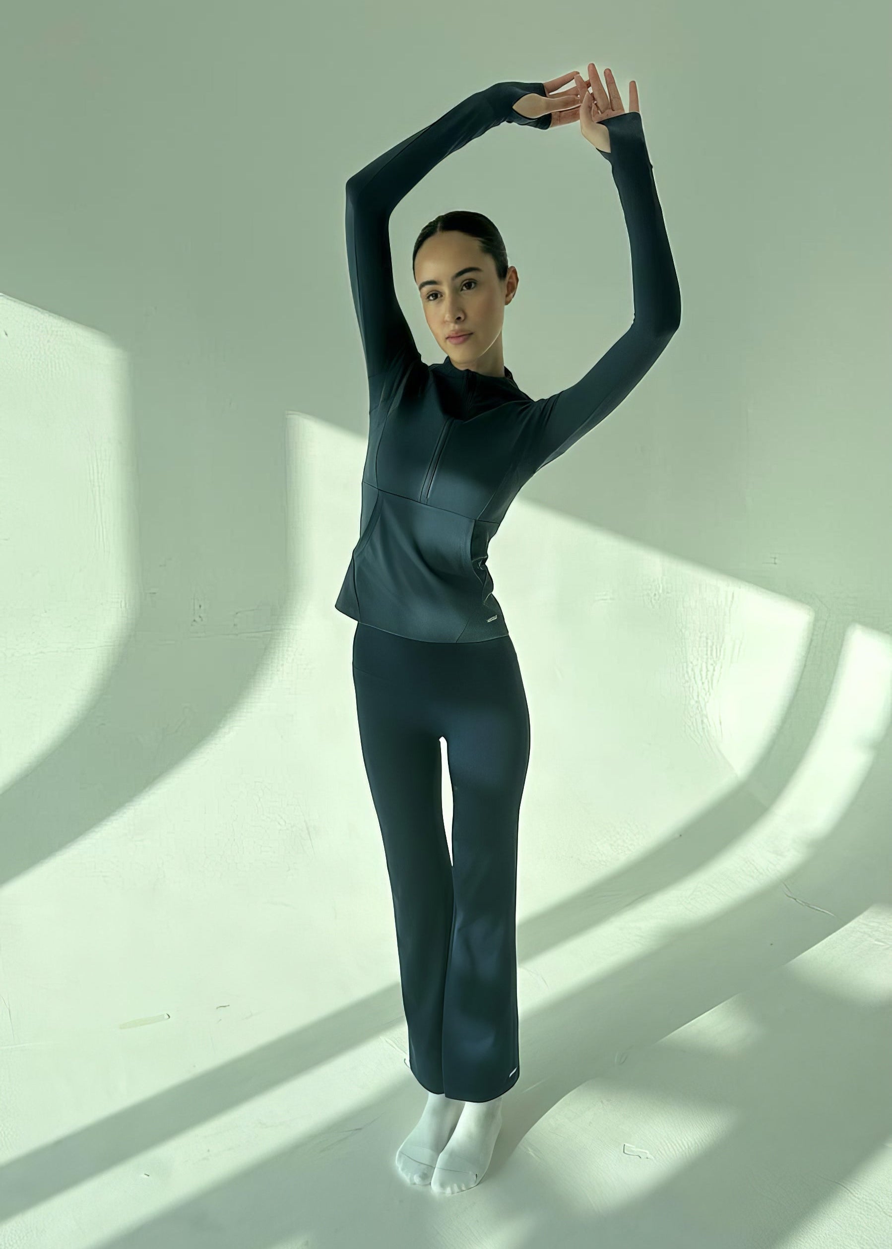 Person in a black outfit standing with one arm raised against a white background