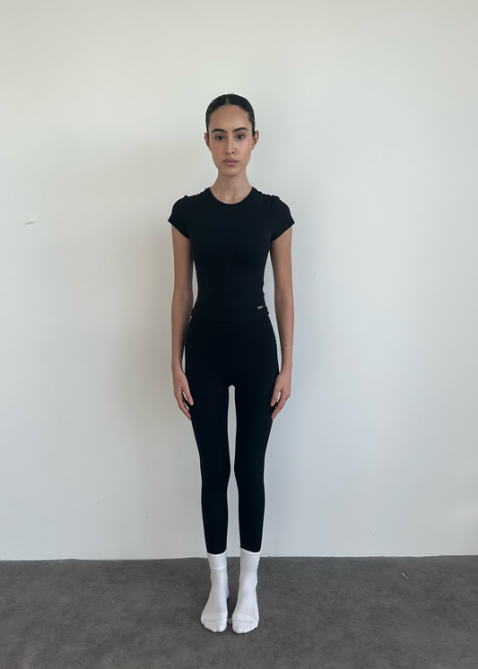 Person wearing a black outfit standing against a white wall.