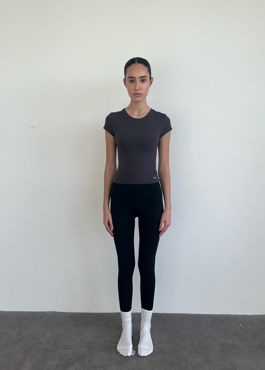 Person wearing a black t-shirt and leggings standing against a white wall.