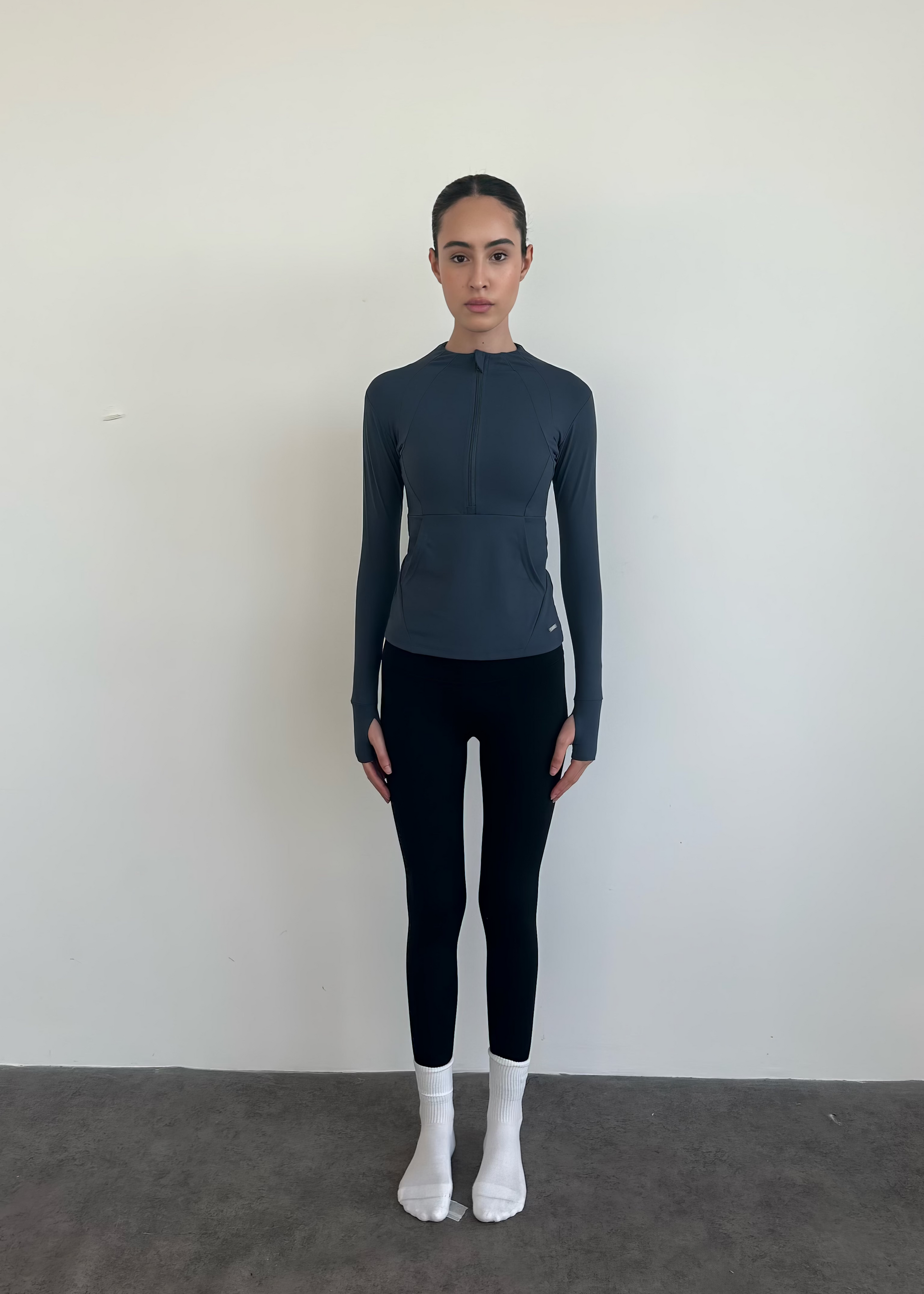 Person wearing a dark gray long-sleeve top and black leggings against a plain background