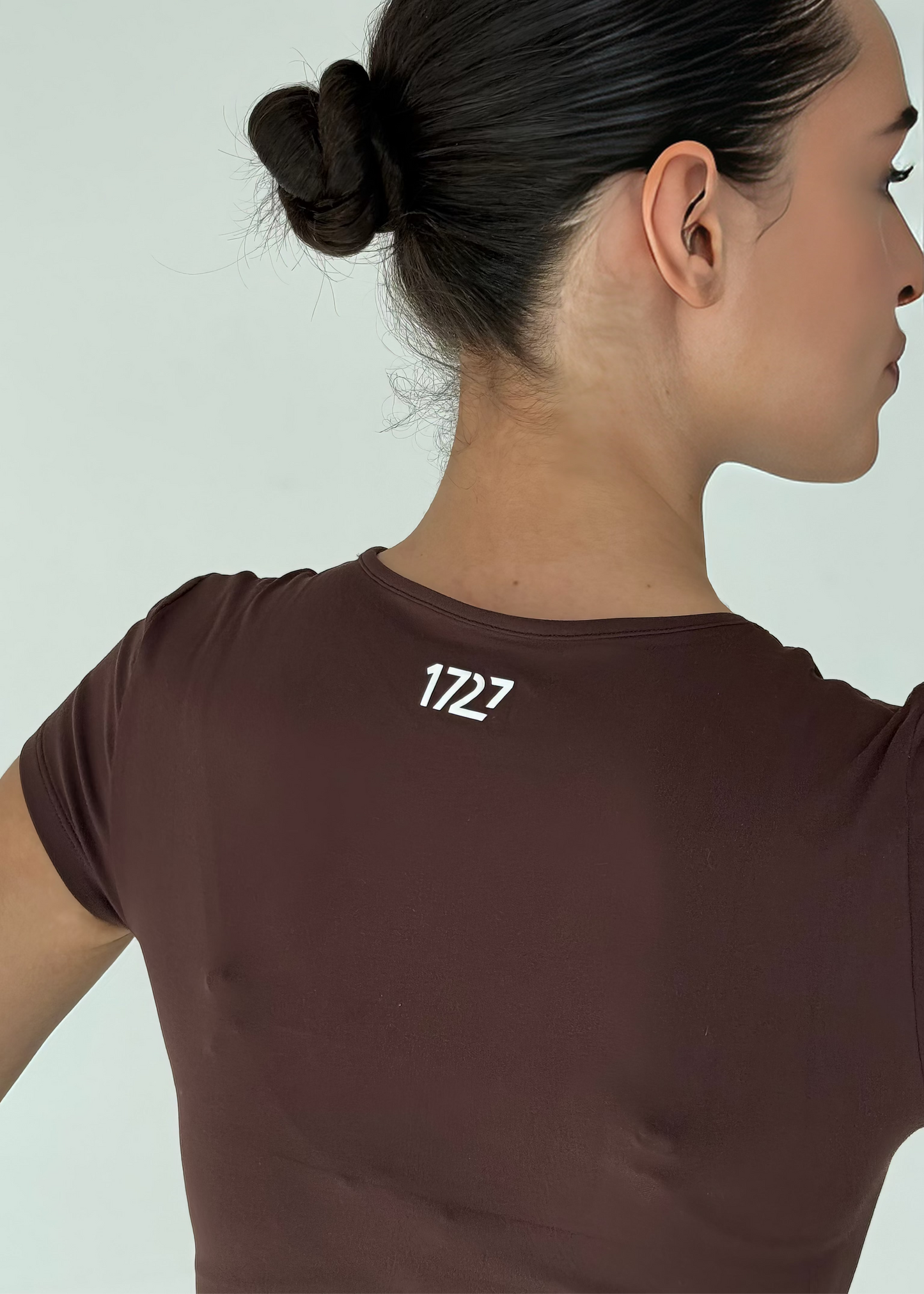 Woman wearing a brown t-shirt with the number 1722 on a light gray background