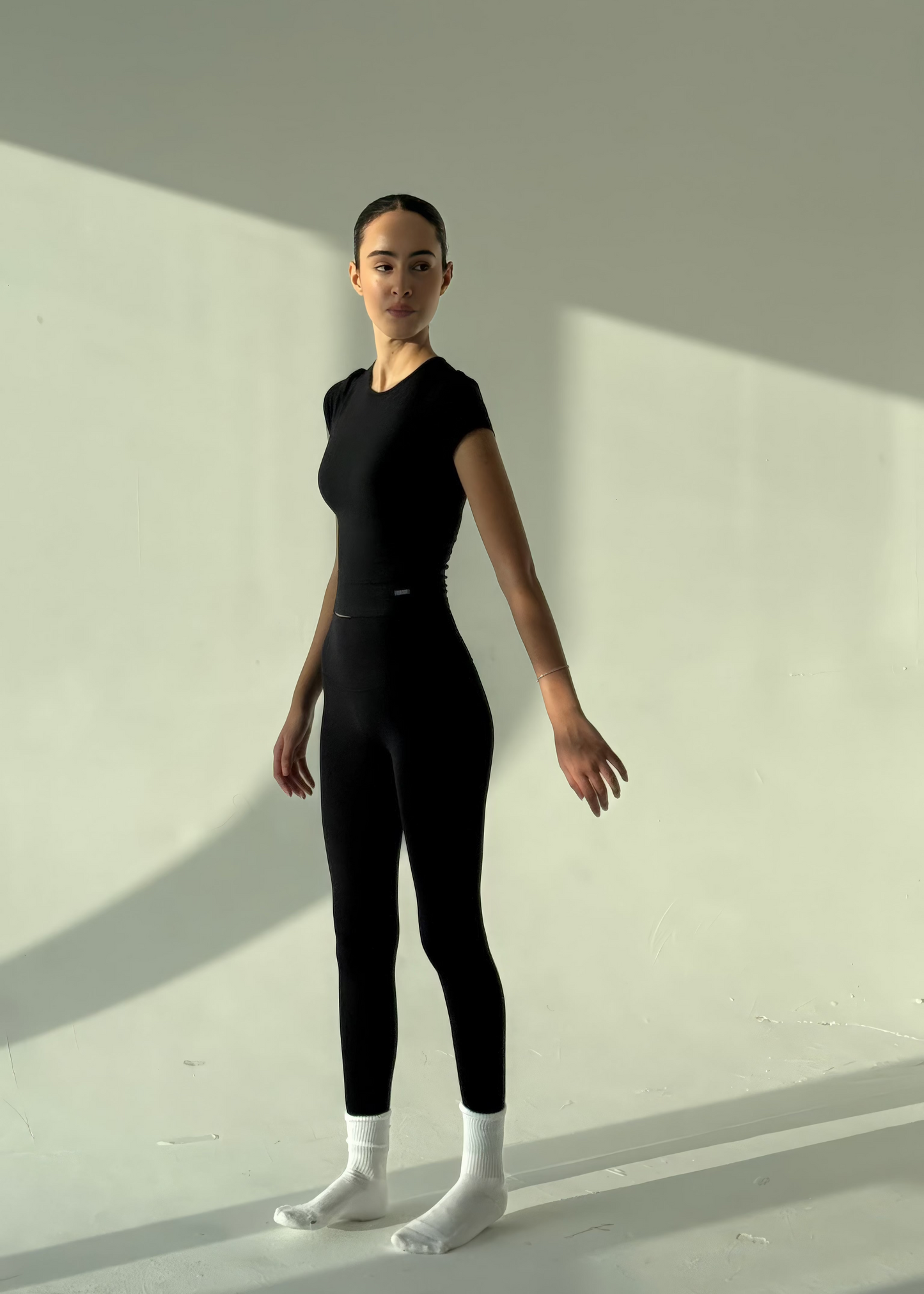 Person wearing a black bodysuit standing against a light background