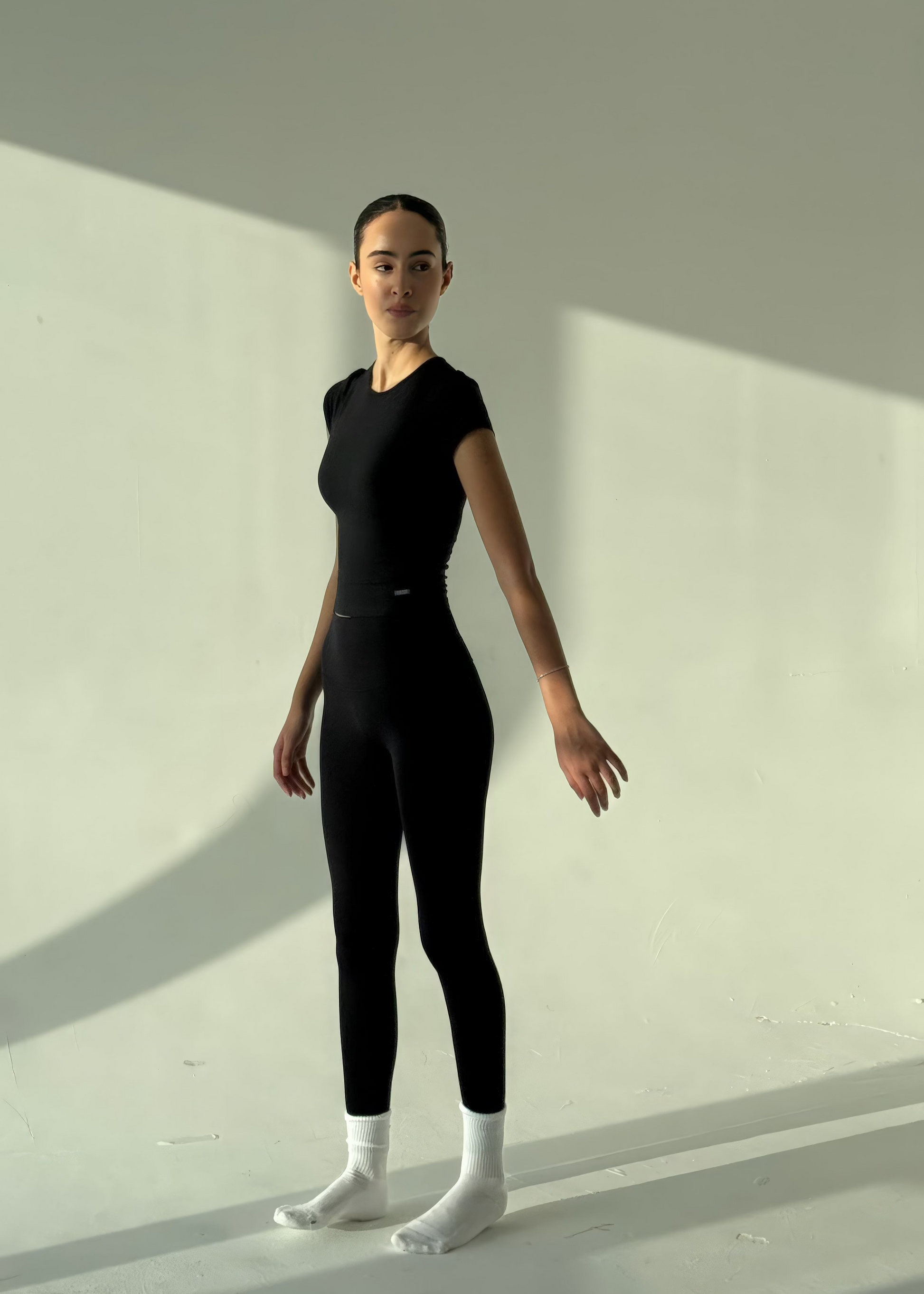 Person wearing a black bodysuit standing against a light background